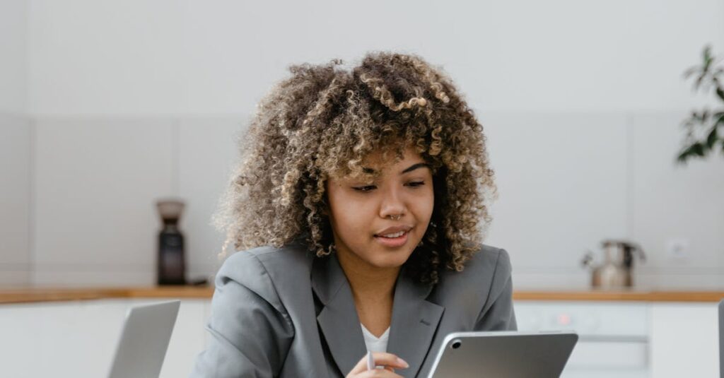 Confident woman using a tablet at a desk with a laptop, enhancing productivity in a modern office.