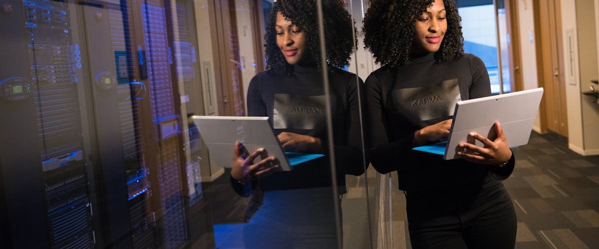 African American woman standing in modern office using laptop, reflecting professionalism and technology engagement.